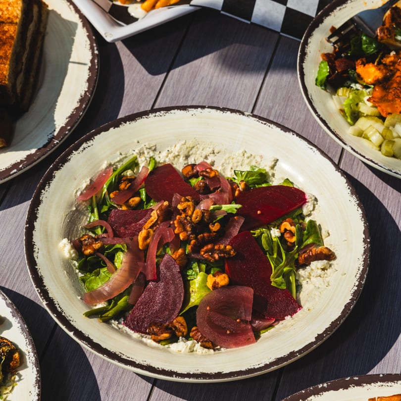 Vibrant beet, walnut, and red onion salad with greens and cheese on a wooden table.