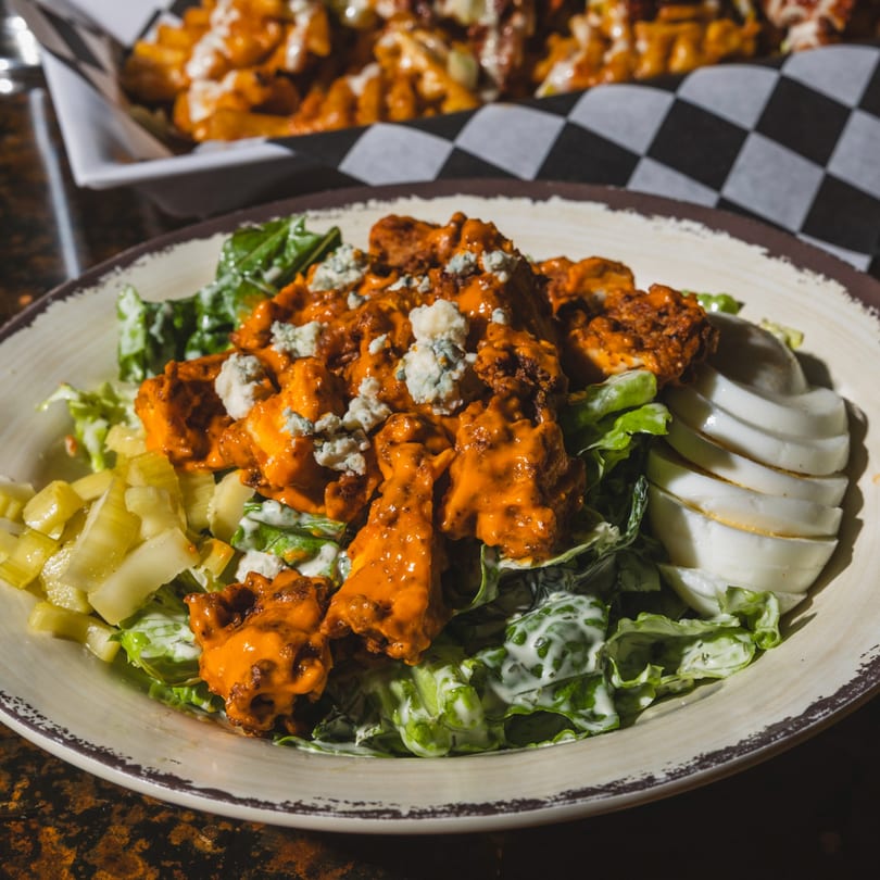 Buffalo chicken salad with blue cheese, lettuce, celery, and sliced eggs on a rustic plate.