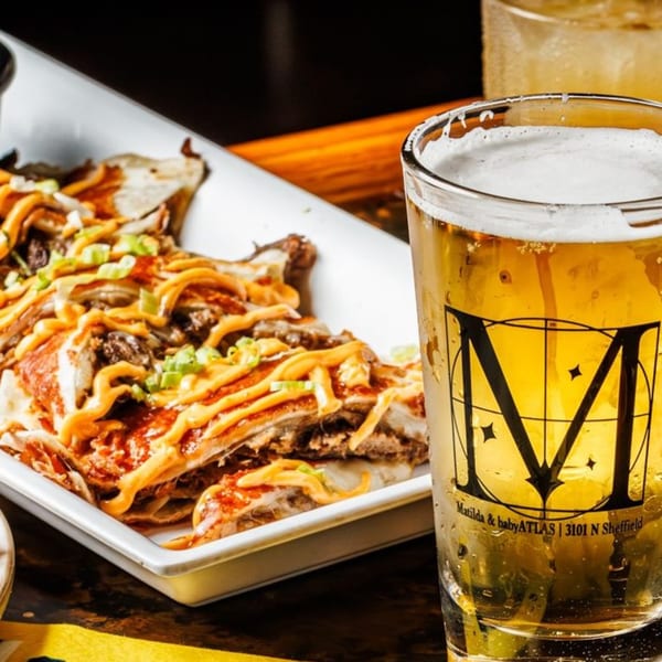 Matilda's loaded nachos with cheese, meat, and green onions, next to a branded glass of beer.