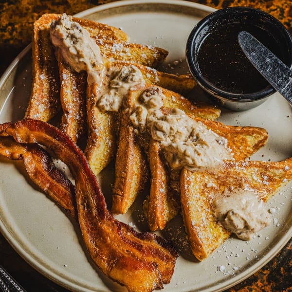 Matilda's French toast with powdered sugar, bacon, gravy, and a side of syrup.