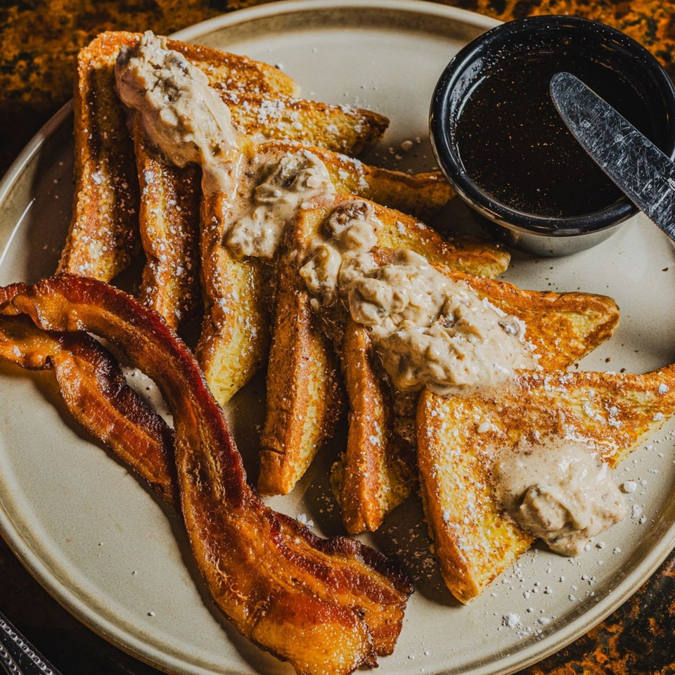 Matilda's French toast with powdered sugar, bacon, gravy, and a side of syrup.