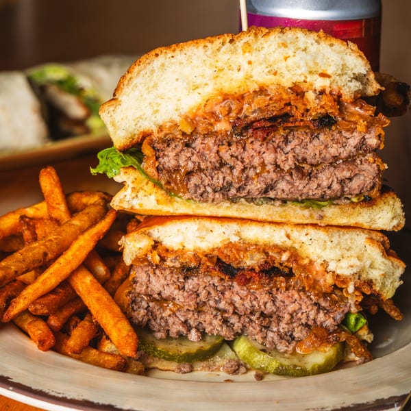 A Matilda burger, cut in half, revealing two patties, caramelized onions, pickles, and a side of fries.